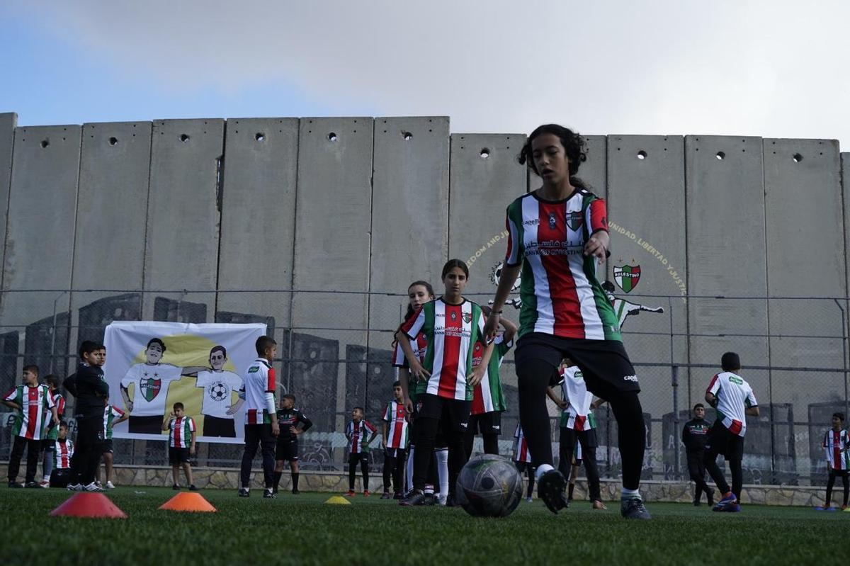 El estadio de fútbol del campamento de refugiados Aida en Belén, con el muro de separación israelí al fondo. (Fuente: El Periódico)