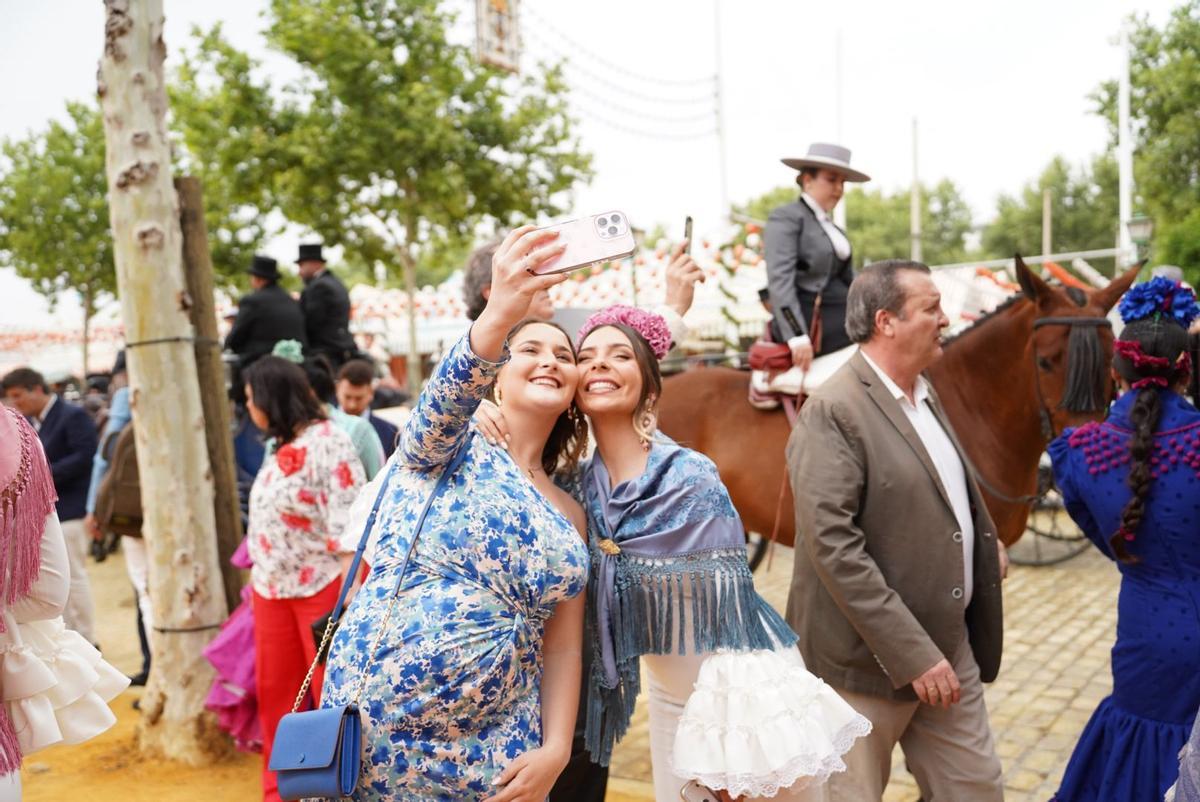 Influencers desfilando por el Real en la Feria de Abril, rodeadas de farolillos y trajes de flamenca.