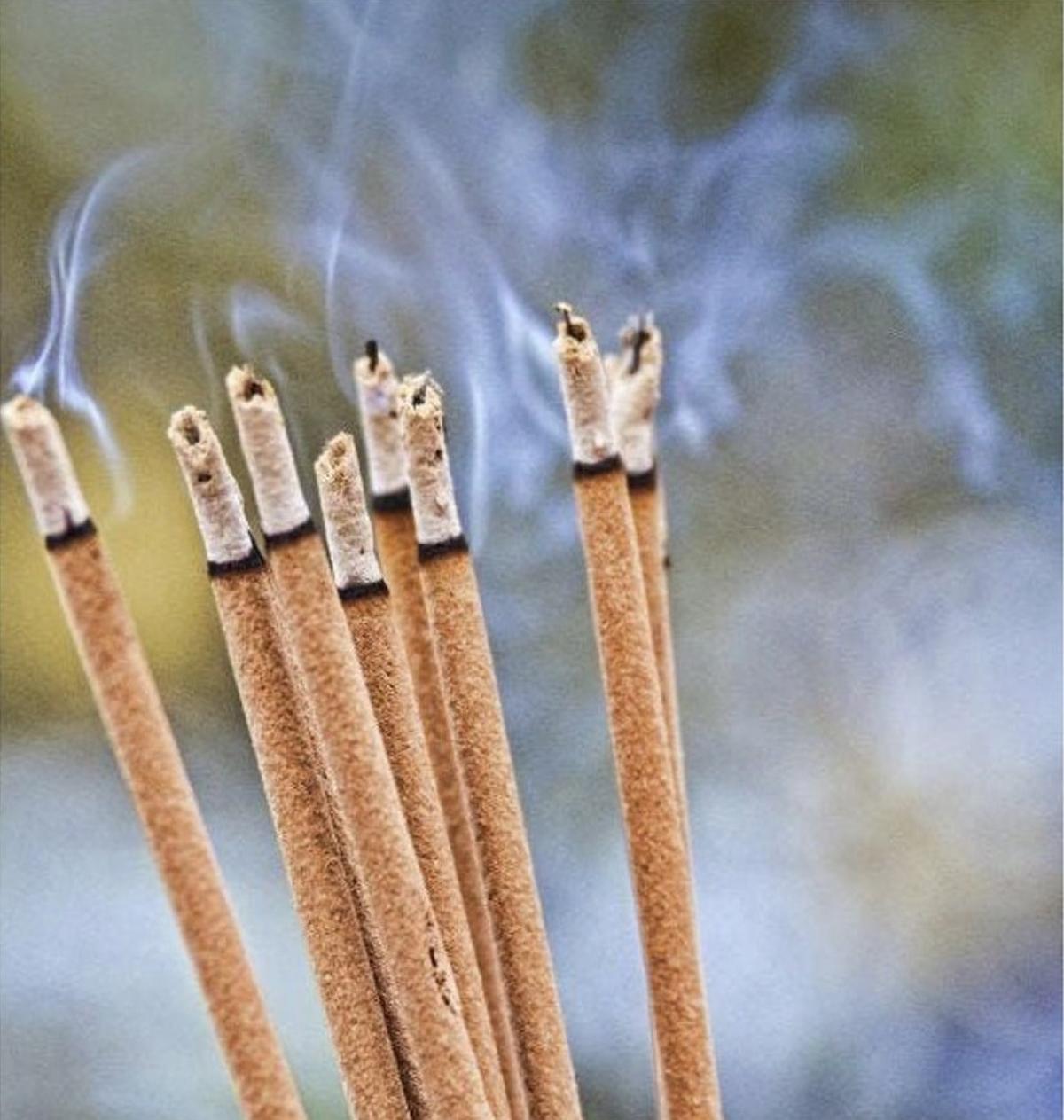 Varilla de incienso encendida, con humo elevándose en un ambiente interior