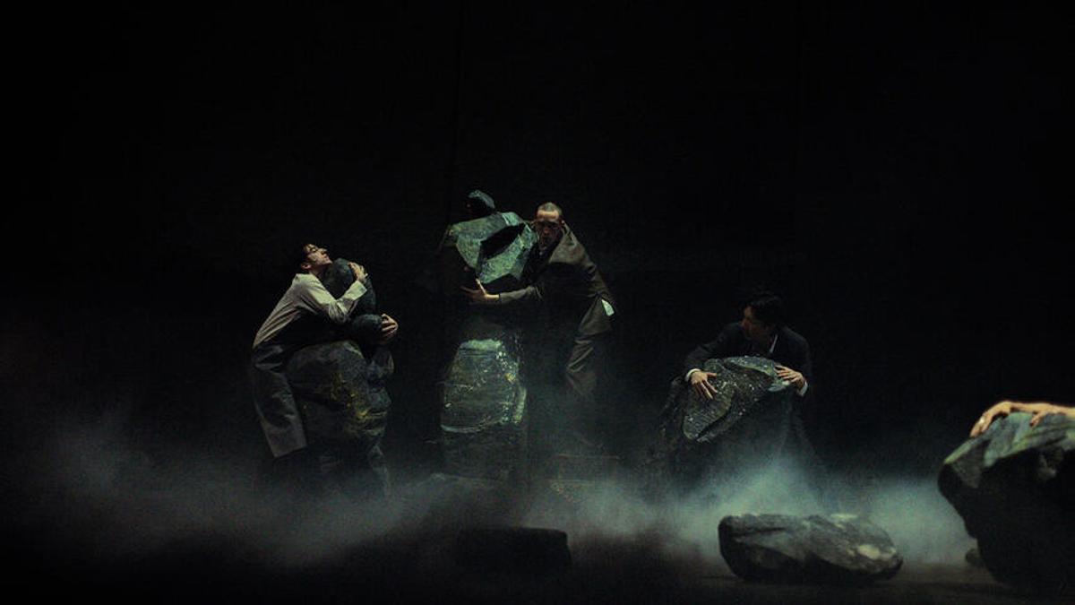 Escena de 'Chroniques' con bailarines rodeados de piedras y luces tenues