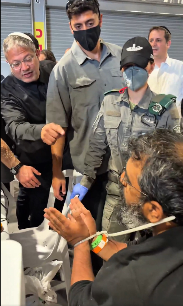 Itamar Ben Gvir sonríe mientras muestra una bandera israelí frente a activistas atados en el puerto de Ashdod